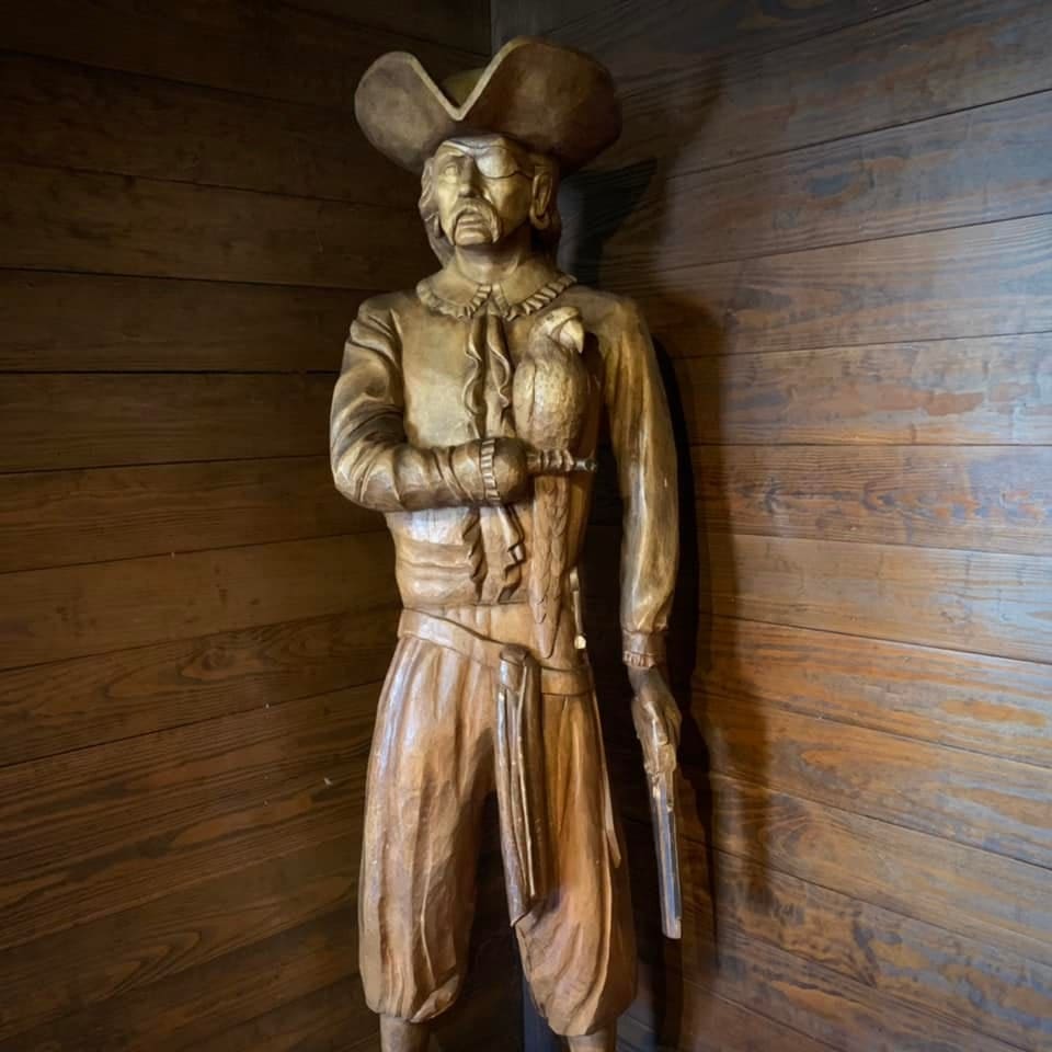 A wooden statue of a pirate holding a parrot and a pistol stands against a wooden wall in the historic district of Savannah, Georgia.