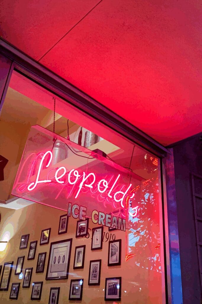 A neon sign for Leopold's Ice Cream, established in 1910, glows in the historic district of Savannah, Georgia, with framed photographs visible in the shop's window.