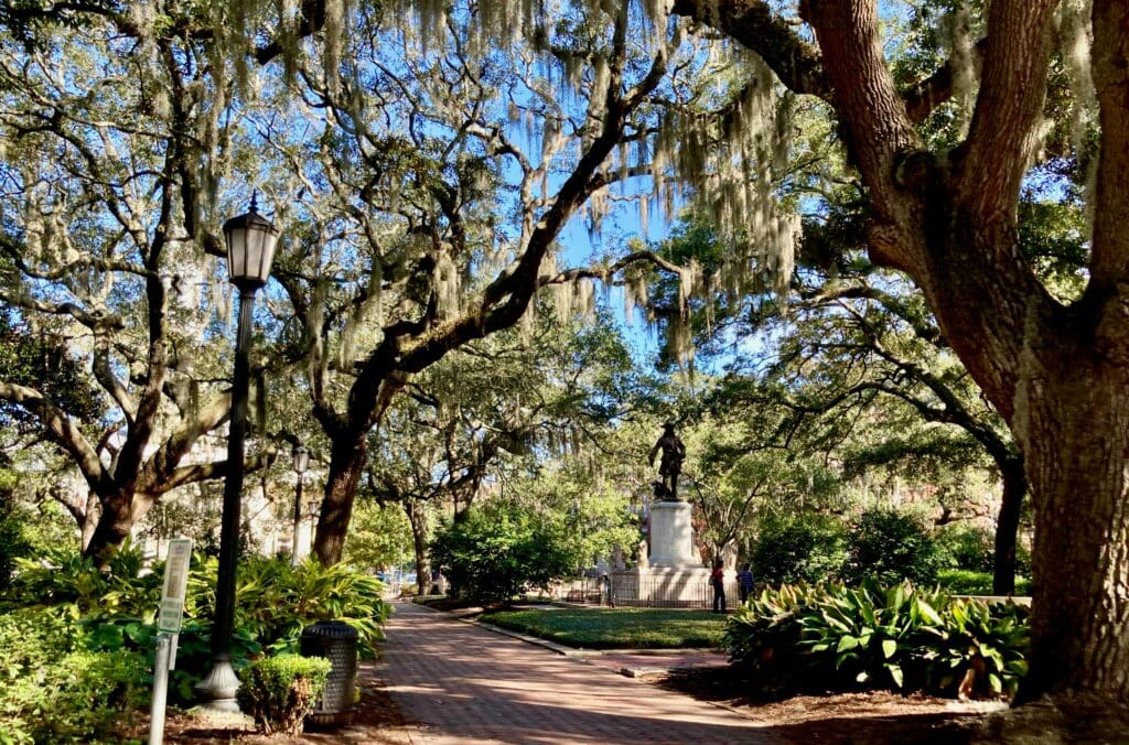 A statue of a historical figure stands on a pedestal in Chippewa Square surrounded by decorative elements in the historic district of Savannah, Georgia.