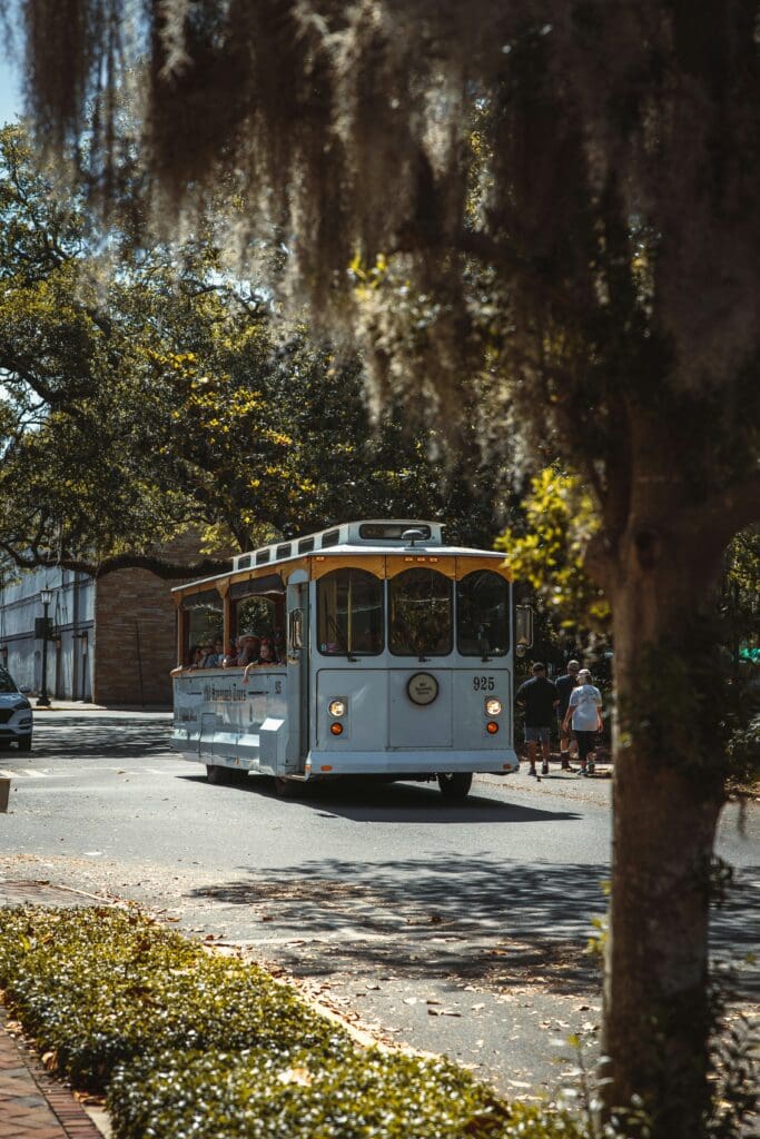 A historic trolley car drives through the streets of the historic district of Savannah, Georgia, with passengers enjoying the view.