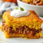 Mexican Corn Bread sitting on a white plate with a bowl of chili in the background