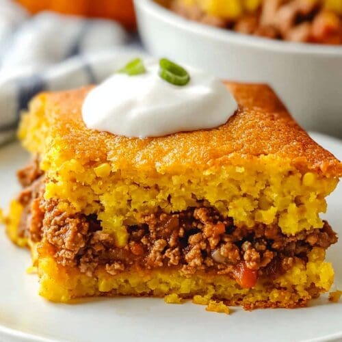 Mexican Corn Bread sitting on a white plate with a bowl of chili in the background